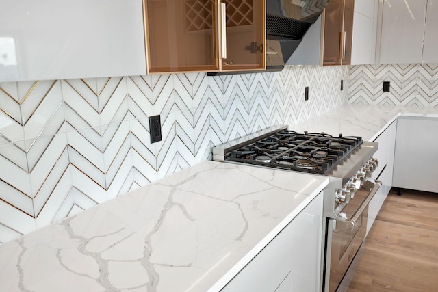 kitchen with backsplash, stainless steel range, light stone counters, and light hardwood / wood-style flooring