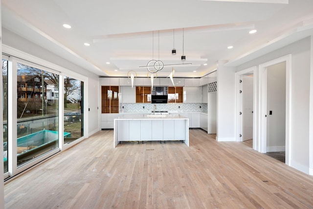 kitchen featuring a kitchen island, decorative light fixtures, white cabinetry, decorative backsplash, and a tray ceiling