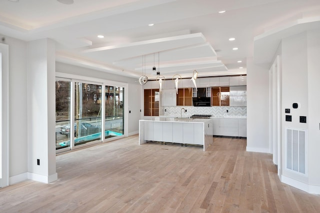 kitchen with pendant lighting, a large island, a tray ceiling, and light hardwood / wood-style floors