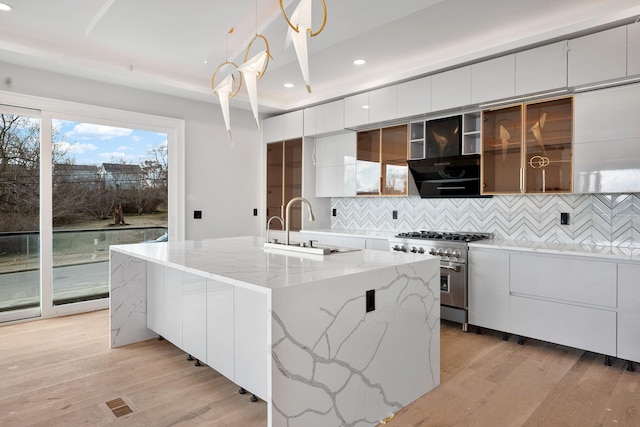 kitchen featuring sink, high end stainless steel range oven, an island with sink, white cabinets, and decorative light fixtures