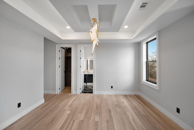 interior space with ensuite bath, light hardwood / wood-style flooring, and a raised ceiling