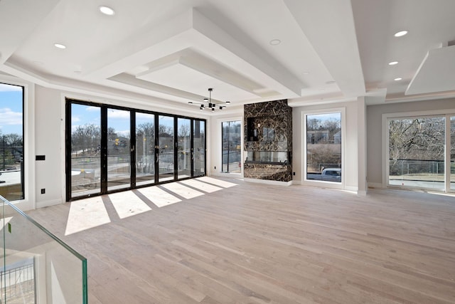 unfurnished living room with a healthy amount of sunlight, a tray ceiling, a premium fireplace, and light wood-type flooring