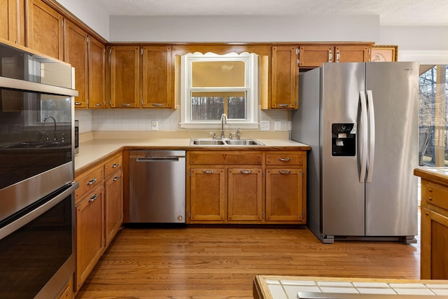 kitchen with a wealth of natural light, tasteful backsplash, sink, stainless steel appliances, and light wood-type flooring