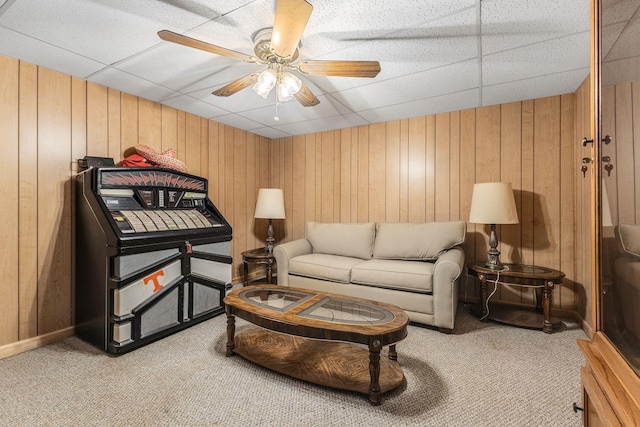 carpeted living room with ceiling fan, a drop ceiling, and wooden walls