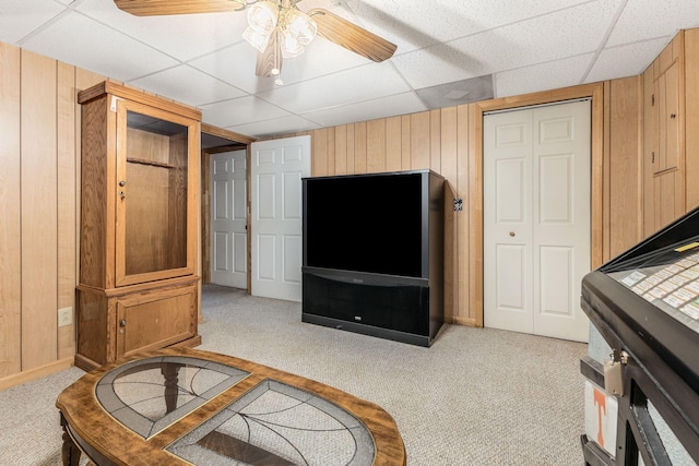 carpeted living room featuring ceiling fan, wooden walls, and a drop ceiling