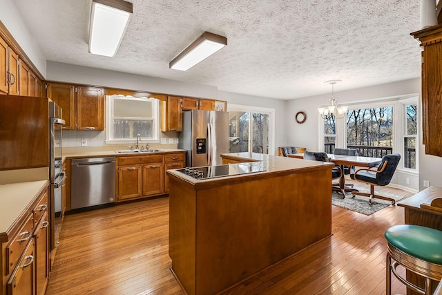 kitchen featuring pendant lighting, appliances with stainless steel finishes, a center island, light hardwood / wood-style floors, and a healthy amount of sunlight