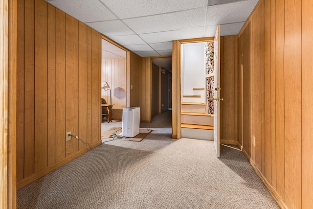 interior space with a drop ceiling, carpet, and wood walls