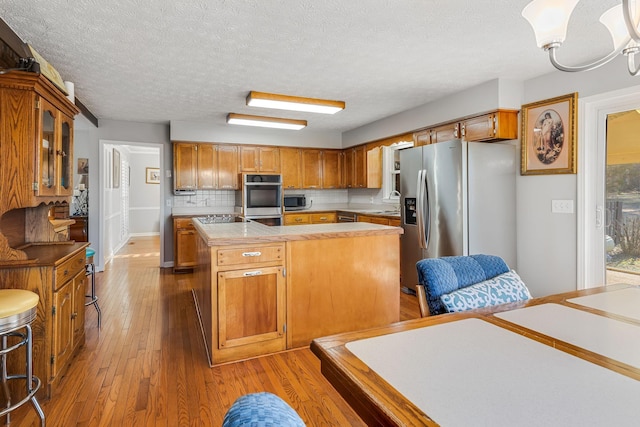 kitchen featuring a textured ceiling, a kitchen island, hardwood / wood-style flooring, stainless steel appliances, and backsplash