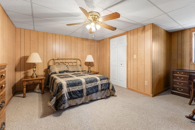 bedroom featuring a paneled ceiling, ceiling fan, carpet floors, a closet, and wood walls