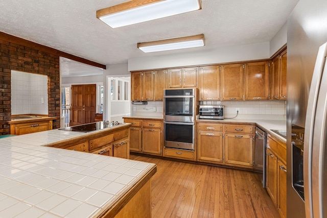 kitchen featuring appliances with stainless steel finishes, tile countertops, light hardwood / wood-style floors, and backsplash