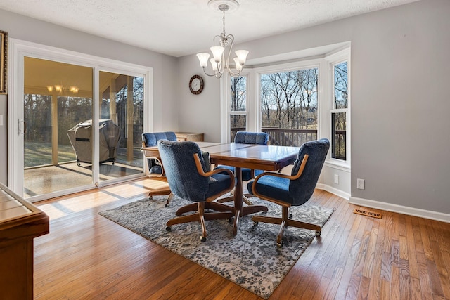 dining space with an inviting chandelier, wood-type flooring, and a textured ceiling