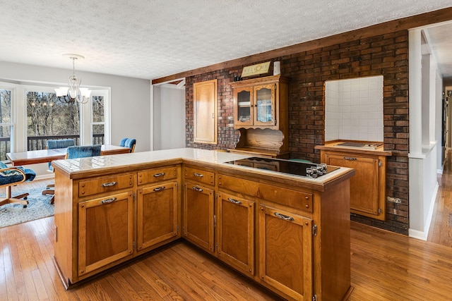 kitchen with black electric cooktop, decorative light fixtures, tile countertops, and light hardwood / wood-style flooring