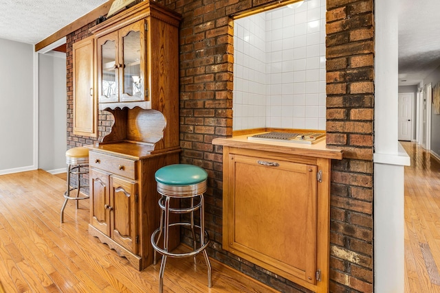 bar with brick wall, a textured ceiling, and light wood-type flooring