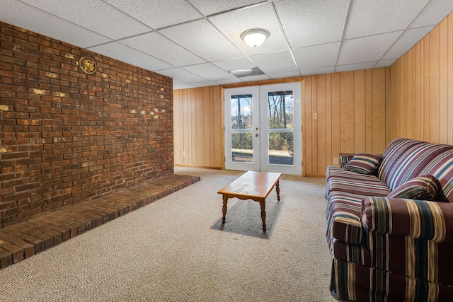 living room featuring wood walls, light colored carpet, a drop ceiling, and french doors