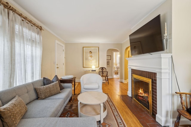 living room with crown molding, wood-type flooring, and a brick fireplace