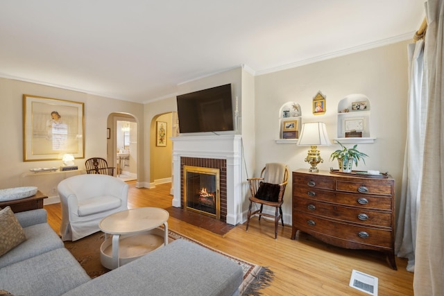 living room with crown molding, a brick fireplace, and light wood-type flooring