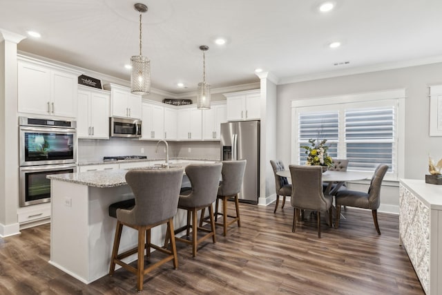 kitchen featuring pendant lighting, white cabinetry, an island with sink, ornamental molding, and stainless steel appliances