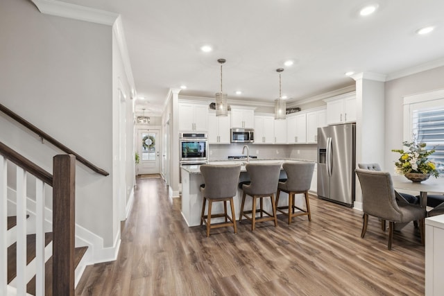 kitchen with pendant lighting, crown molding, appliances with stainless steel finishes, white cabinetry, and an island with sink