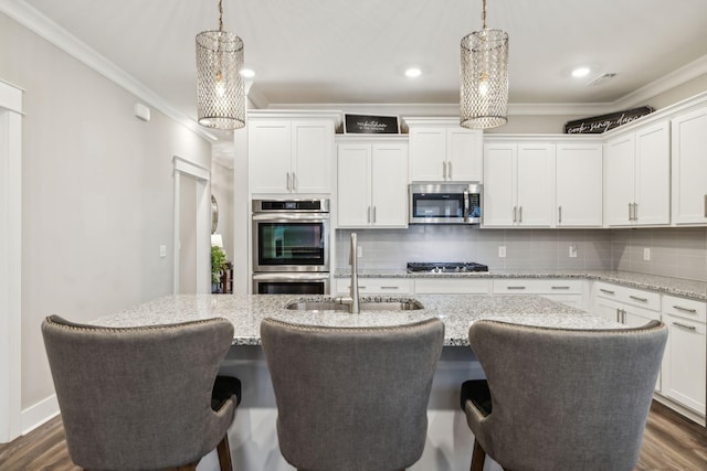 kitchen featuring white cabinetry, appliances with stainless steel finishes, a center island with sink, and decorative light fixtures