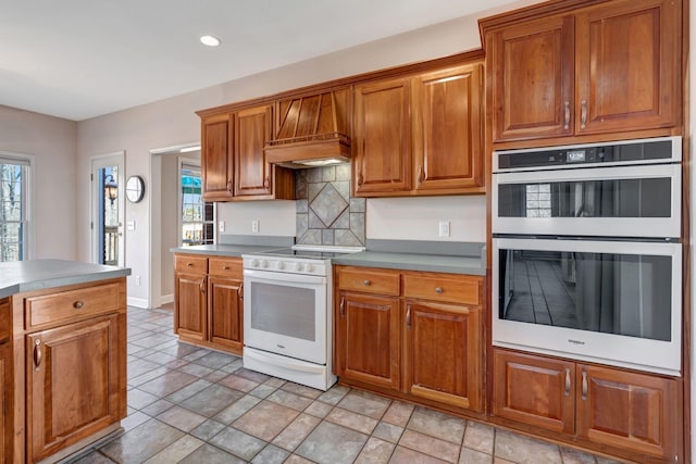 kitchen with decorative backsplash, white appliances, a healthy amount of sunlight, and custom range hood