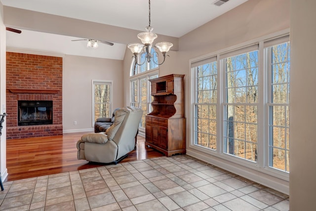 sitting room with a brick fireplace, ceiling fan with notable chandelier, vaulted ceiling, and light tile patterned floors