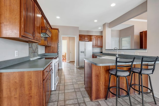 kitchen featuring sink, white appliances, tasteful backsplash, a kitchen bar, and kitchen peninsula