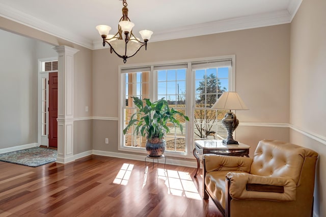 sitting room featuring crown molding, a chandelier, hardwood / wood-style floors, and ornate columns