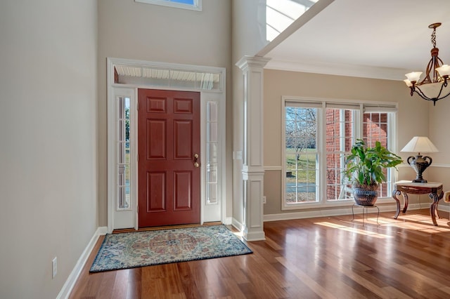 entrance foyer with ornate columns, wood-type flooring, ornamental molding, and a notable chandelier