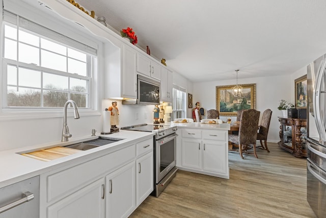 kitchen featuring pendant lighting, white cabinetry, sink, kitchen peninsula, and stainless steel appliances