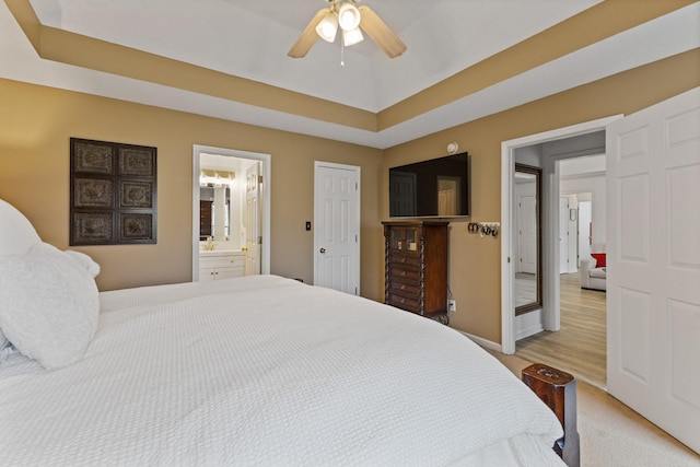 bedroom with a raised ceiling, connected bathroom, ceiling fan, and light hardwood / wood-style flooring