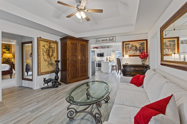 living room with ceiling fan, light hardwood / wood-style floors, and a tray ceiling