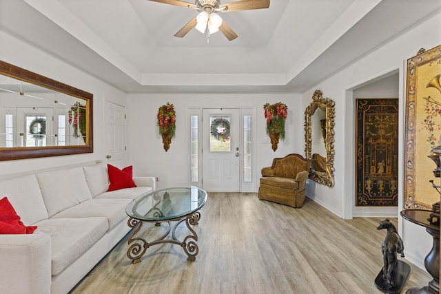 living room with light hardwood / wood-style floors, a raised ceiling, and ceiling fan