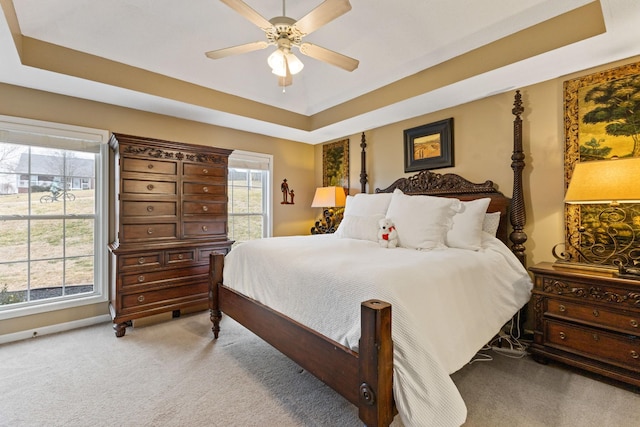 carpeted bedroom with a raised ceiling and ceiling fan