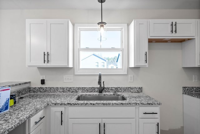 kitchen featuring white cabinetry, light stone countertops, sink, and decorative light fixtures