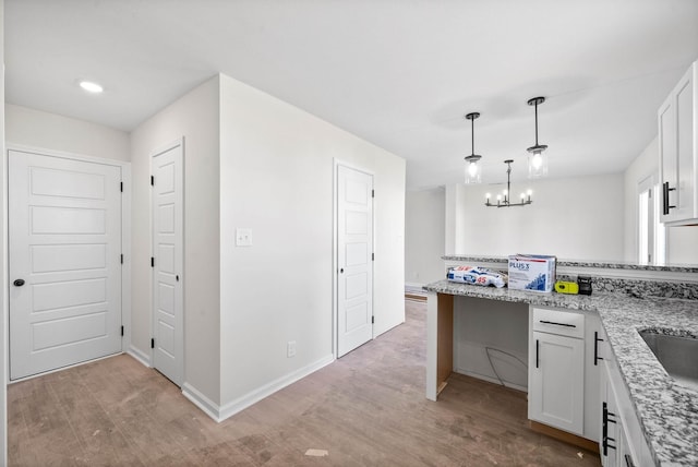 kitchen with white cabinetry, decorative light fixtures, light stone countertops, and light hardwood / wood-style floors