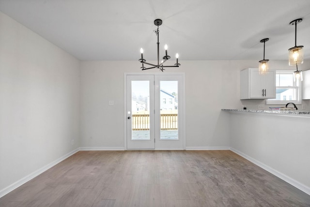 unfurnished dining area featuring sink, light hardwood / wood-style flooring, and a chandelier