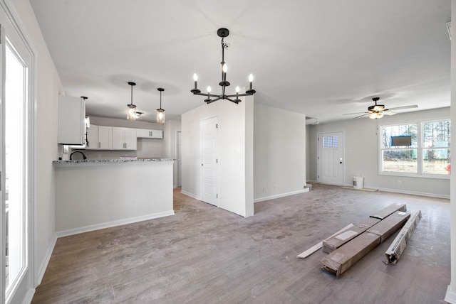 interior space with hanging light fixtures, light wood-type flooring, kitchen peninsula, ceiling fan with notable chandelier, and white cabinets