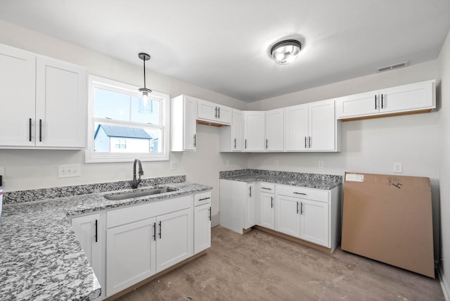 kitchen with white cabinetry, sink, decorative light fixtures, and light wood-type flooring