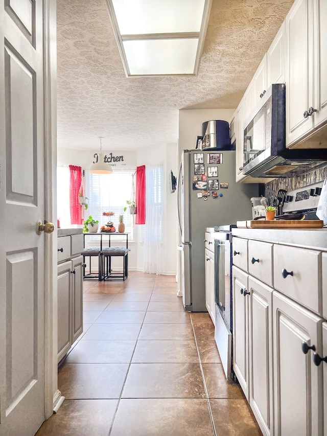 kitchen with stainless steel appliances, tile patterned flooring, a textured ceiling, and white cabinets