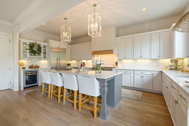 kitchen featuring a breakfast bar, white cabinetry, an island with sink, beverage cooler, and stainless steel built in fridge