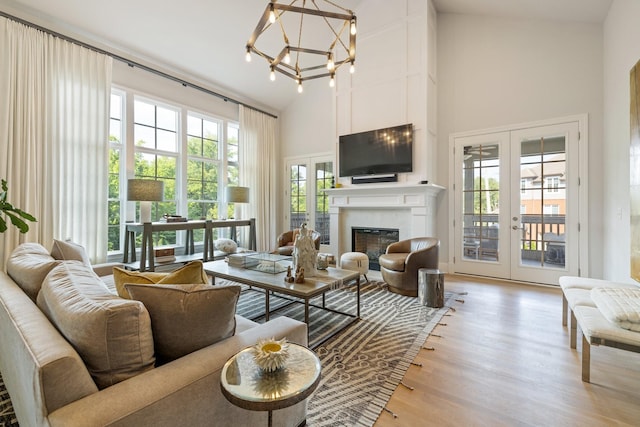 living room with french doors, a chandelier, light hardwood / wood-style flooring, a large fireplace, and a towering ceiling