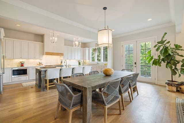 dining space with crown molding, sink, light wood-type flooring, and french doors