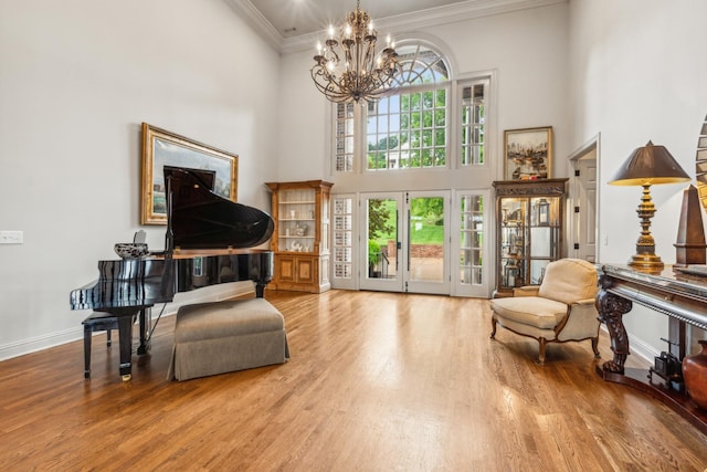 sitting room with crown molding, a towering ceiling, wood-type flooring, and a notable chandelier