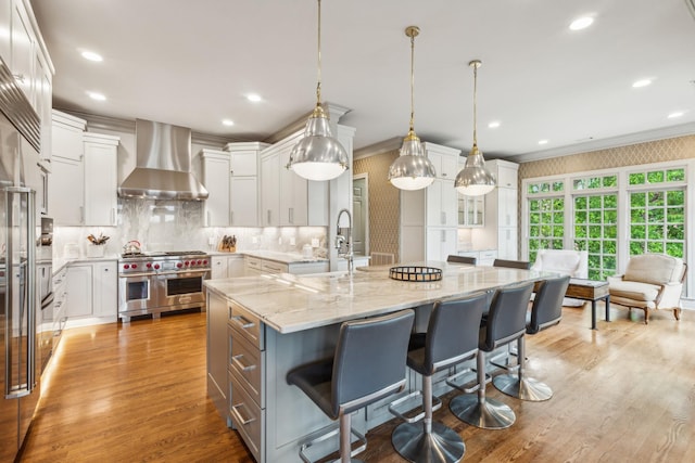 kitchen with a large island, white cabinetry, double oven range, decorative light fixtures, and wall chimney exhaust hood