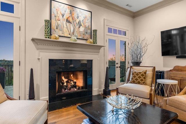 living area featuring hardwood / wood-style floors, crown molding, a fireplace, and french doors