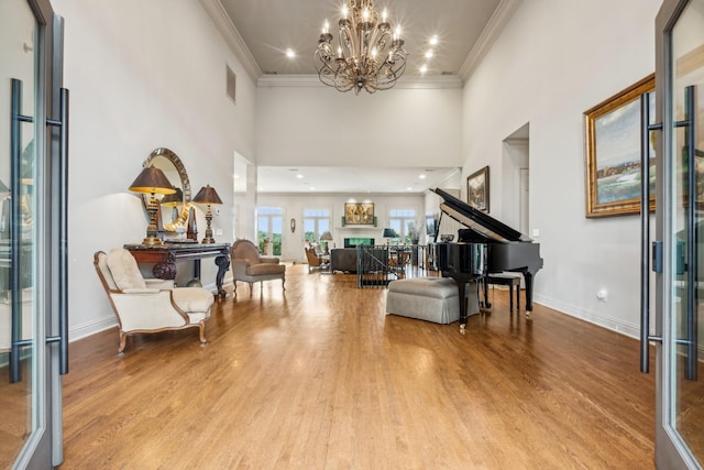 foyer entrance featuring ornamental molding, a towering ceiling, a chandelier, and light hardwood / wood-style floors