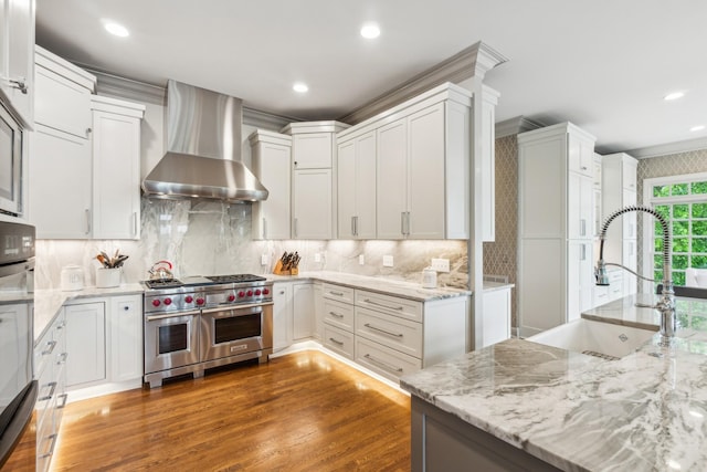 kitchen with white cabinets, sink, range with two ovens, and wall chimney range hood