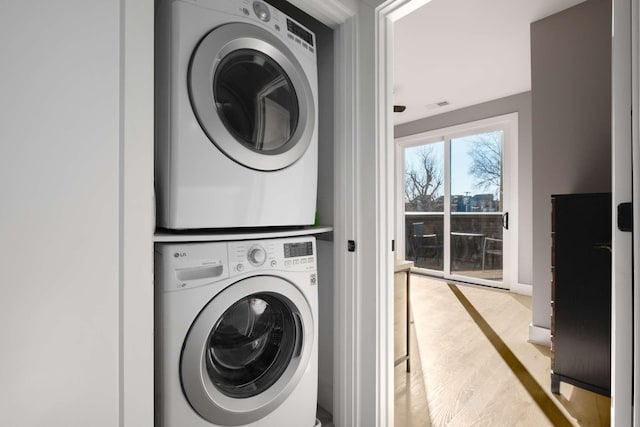 clothes washing area with stacked washing maching and dryer, laundry area, and wood finished floors