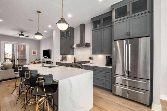 kitchen with high end appliances, open floor plan, light stone countertops, wall chimney range hood, and a sink