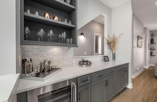 bar featuring wine cooler, baseboards, light wood-style flooring, and decorative backsplash